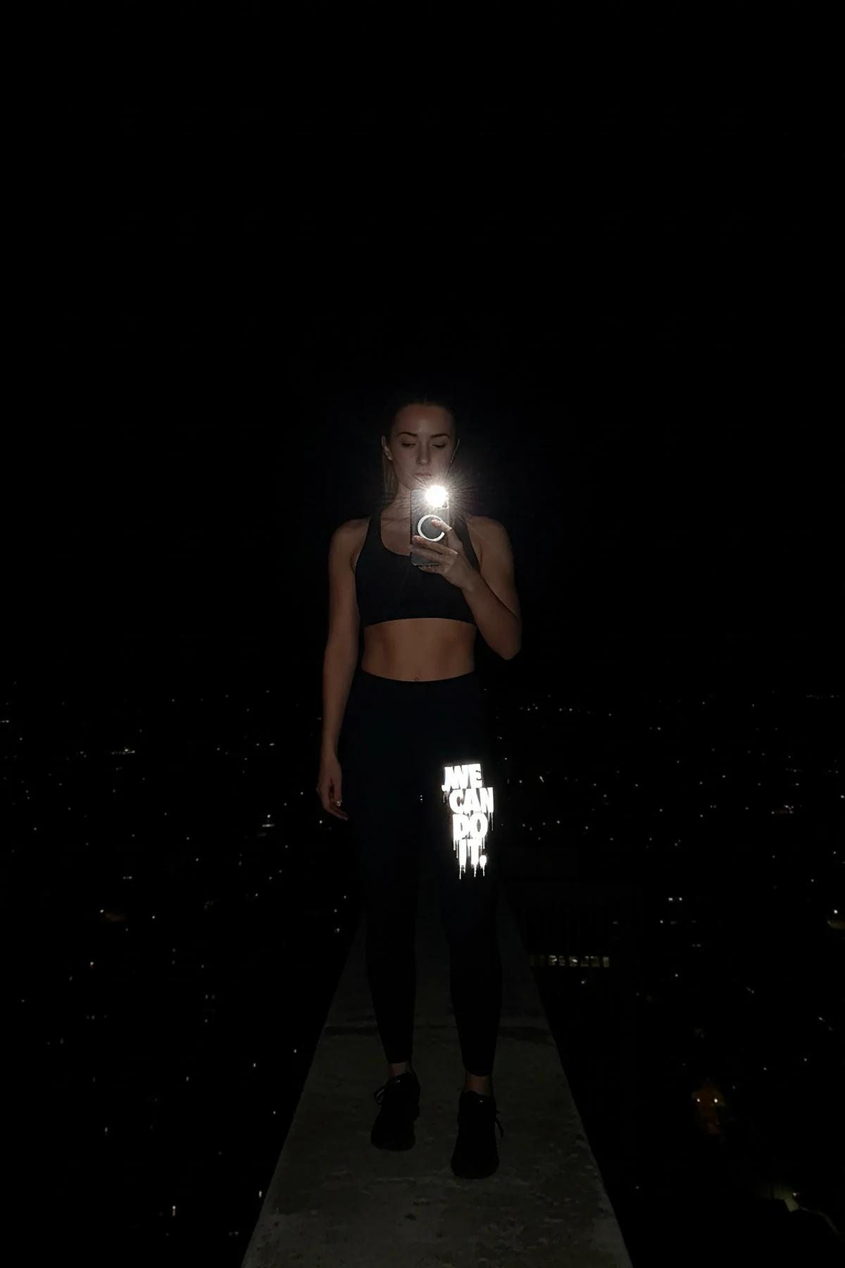 Reflective 'We Can Do It' legging in black with high-visibility print glowing in low light during nighttime cityscape setting
