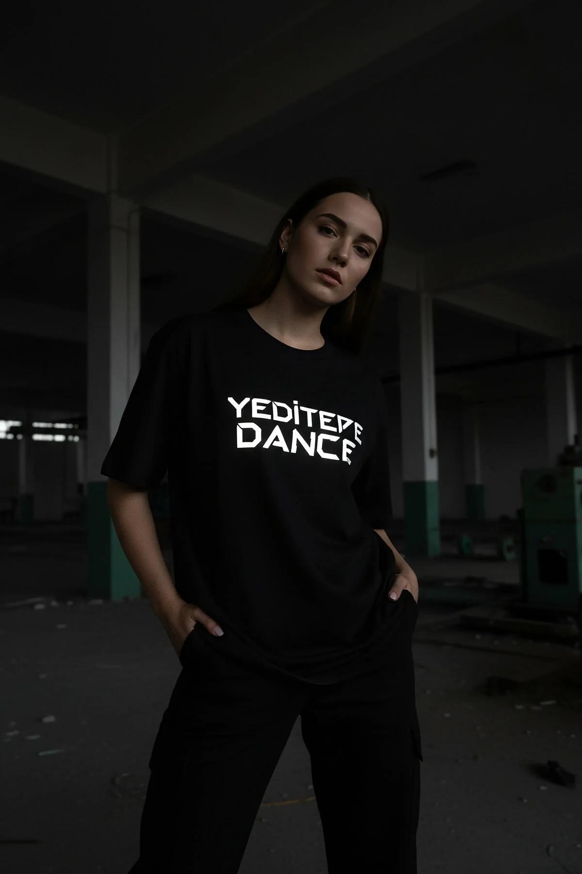 Black cotton t-shirt with a bold white reflective graphic print of 'YEDITEPE DANCE' in the center, worn by a person standing 