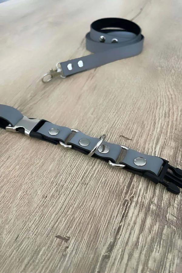 Grey faux leather body harness with silver D-ring snap rivets and detachable snap leash laid flat on wood surface